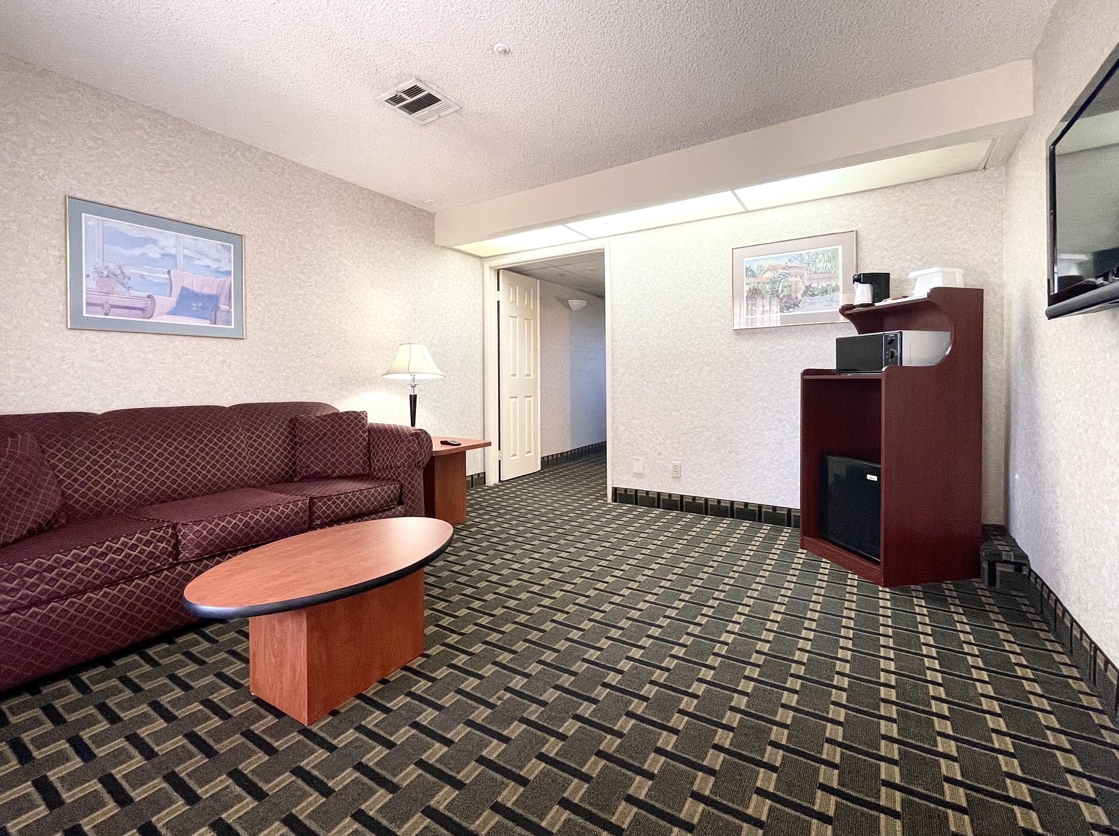 A hotel room with a patterned carpet, a sofa, a small table, a lamp, and a television on a stand.