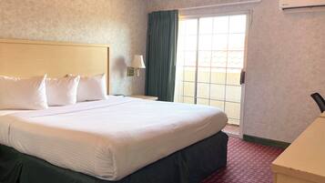 Quarto de hotel com uma cama grande, mesa de cabeceira, abajur, janela com cortinas e ar condicionado.