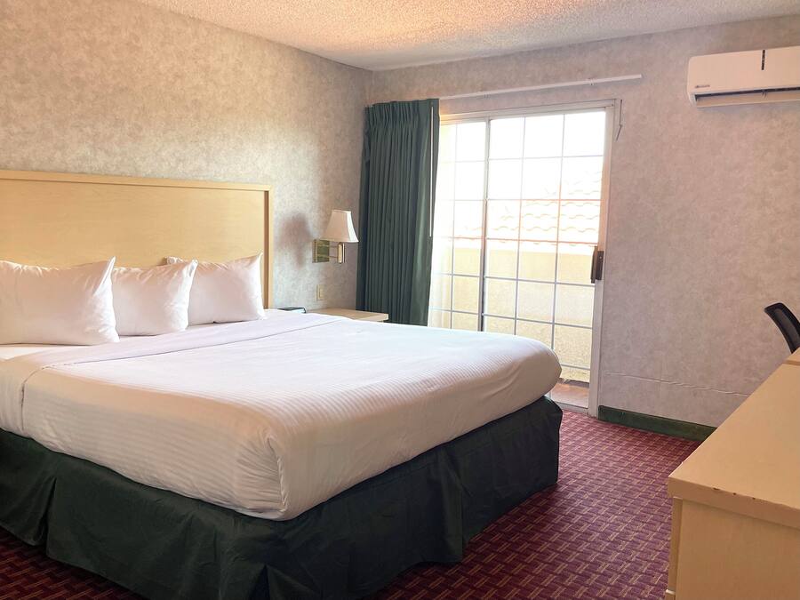 Quarto de hotel com uma cama grande, mesa de cabeceira, abajur, janela com cortinas e ar condicionado.