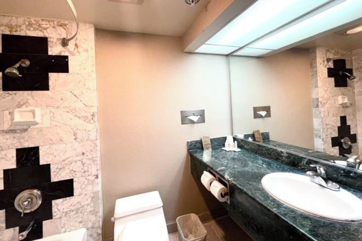 Une salle de bain moderne avec un mur en marbre, un grand miroir, un lavabo et des toilettes.