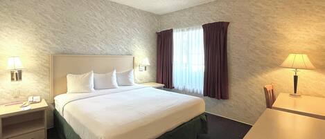 Ett hotellrum med en stor säng, två sängbord med lampor, ett skrivbord och ett fönster med gardiner.
