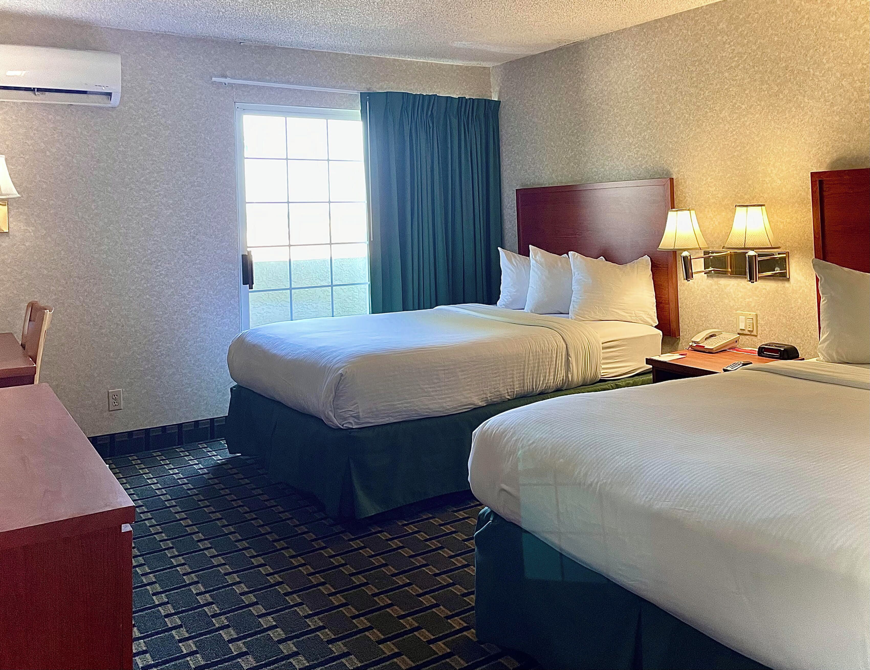 Una habitación de hotel con dos camas, una ventana con cortinas, un escritorio con lámpara y un teléfono en la mesita de noche.