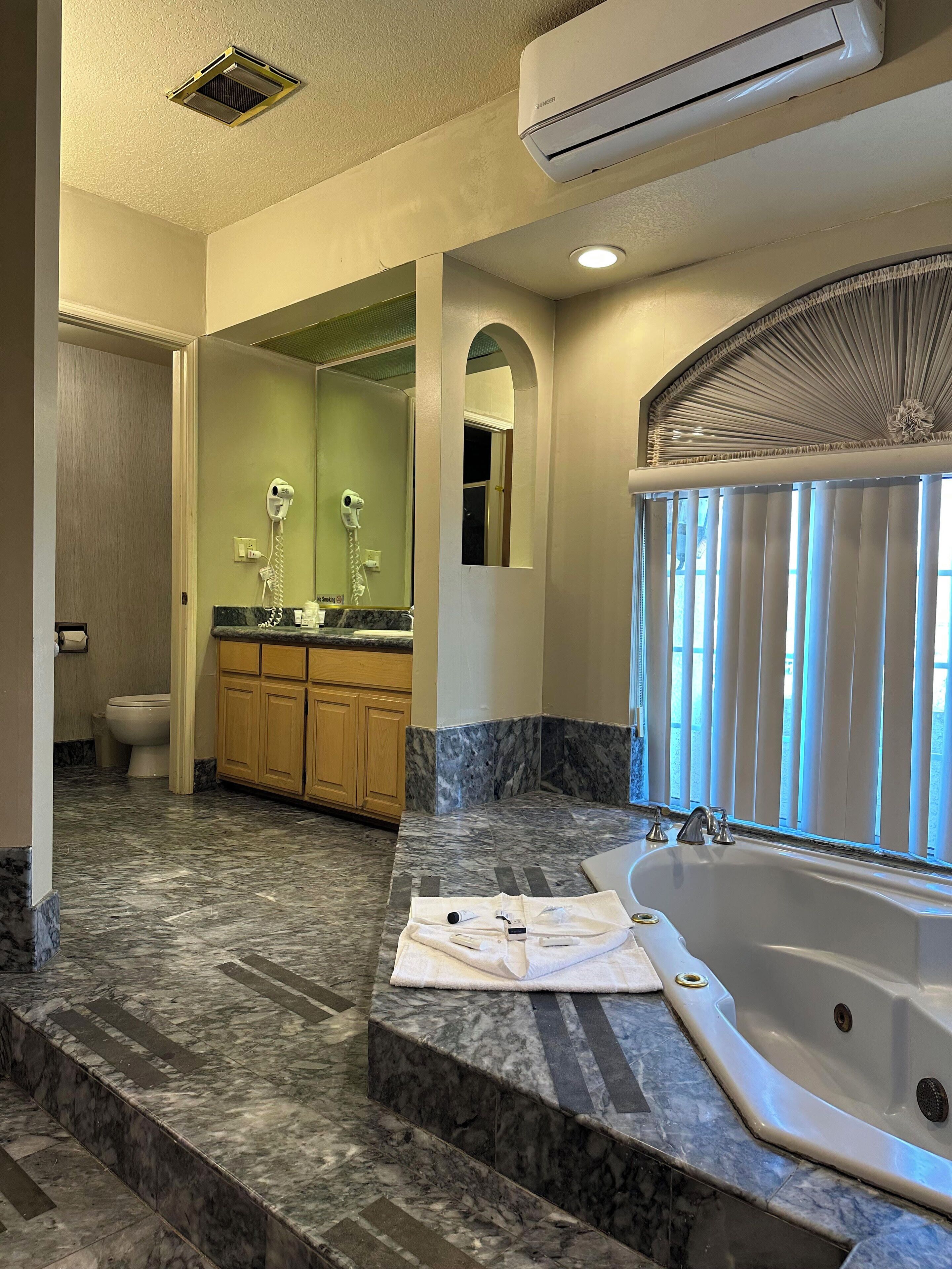 A bathroom with a marble floor, a bathtub, and a vanity with a mirror.