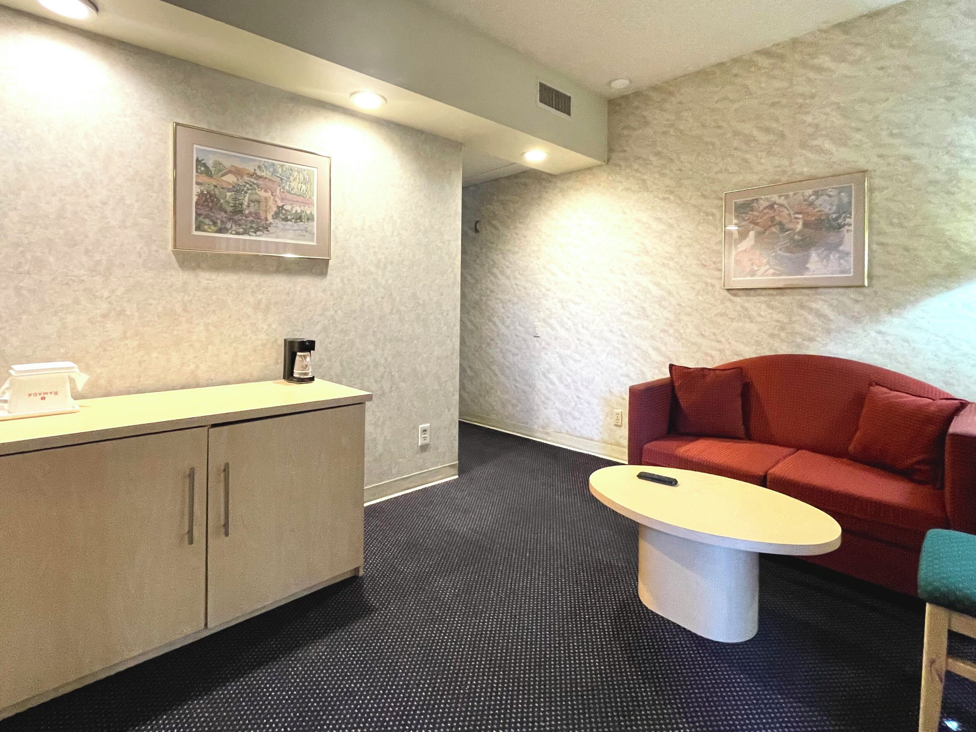 Une chambre d’hôtel avec une kitchenette, un canapé rouge, une petite table ronde et deux tableaux encadrés accrochés aux murs.
