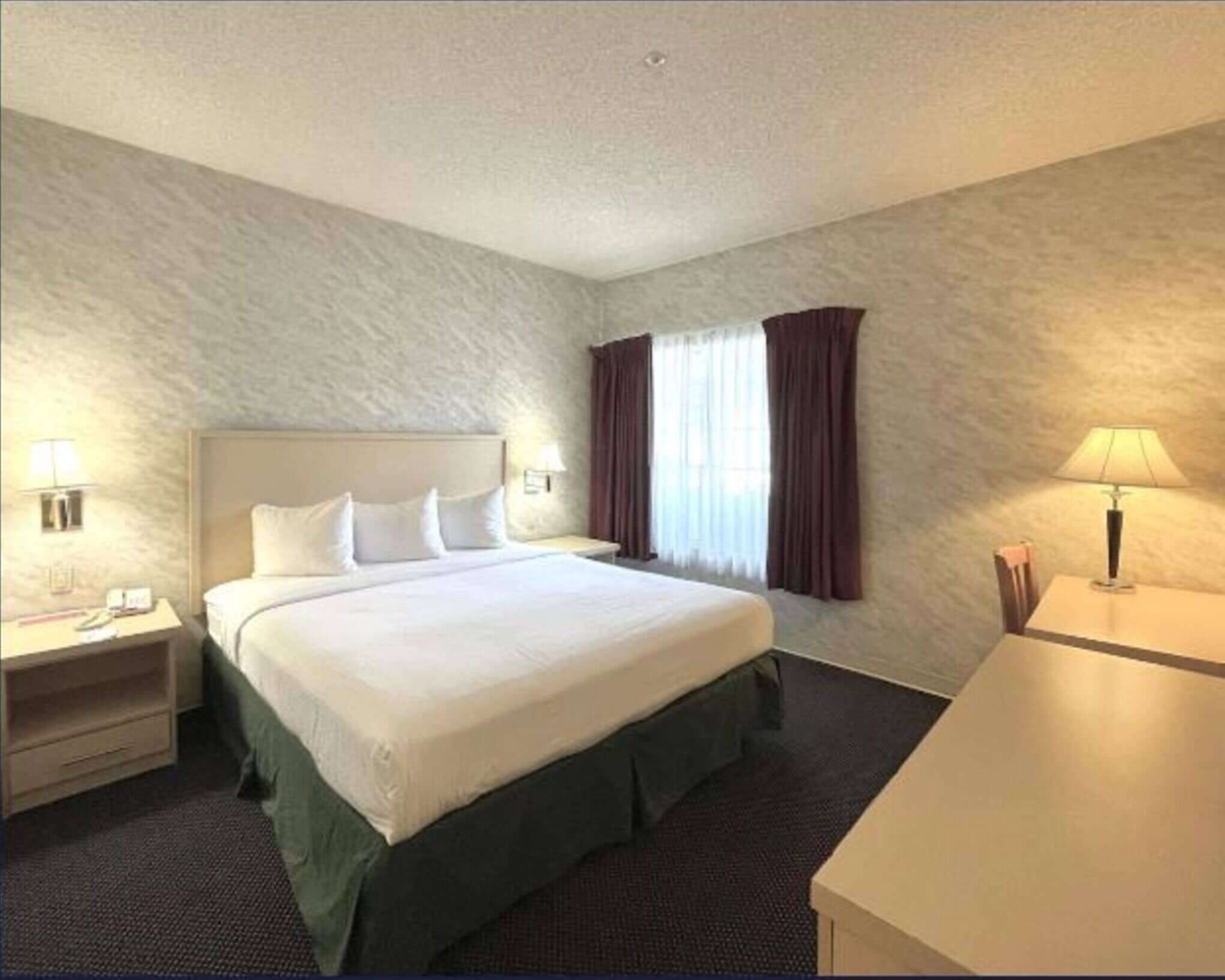 Una habitación de hotel con una cama grande, dos mesitas de noche, un escritorio y una ventana con cortinas.