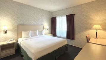 Una habitación de hotel con una cama grande, dos mesitas de noche, un escritorio y una ventana con cortinas.