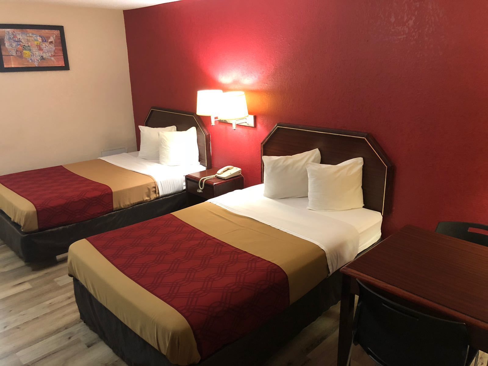 A hotel room with two beds, each with a red and beige bedspread, a wooden headboard, and a nightstand with a telephone.