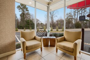 A room with two beige armchairs and a small wooden table, large windows offering a view of trees and a parking lot. - Econo Lodge Williamsburg Historic Area (Williamsburg)