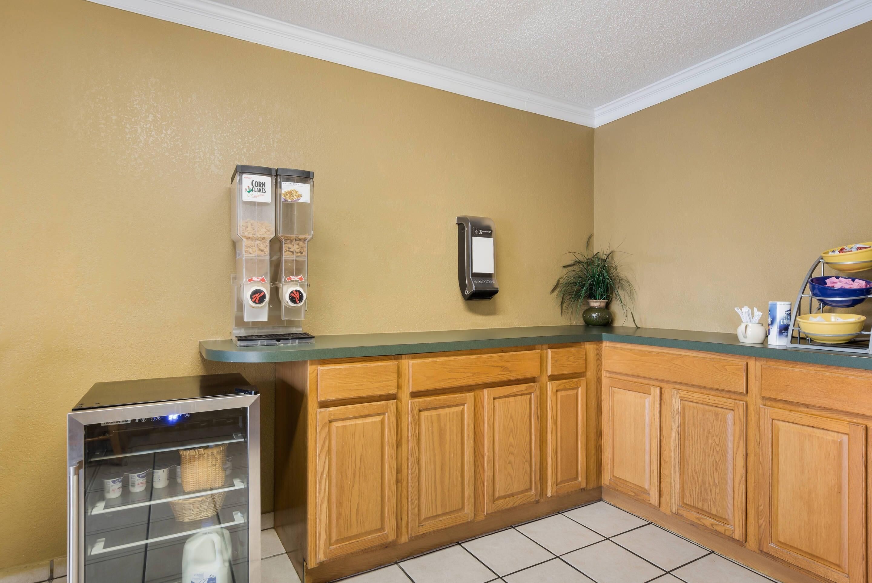 A kitchen with wooden cabinets, a coffee machine, a refrigerator, and a plant.