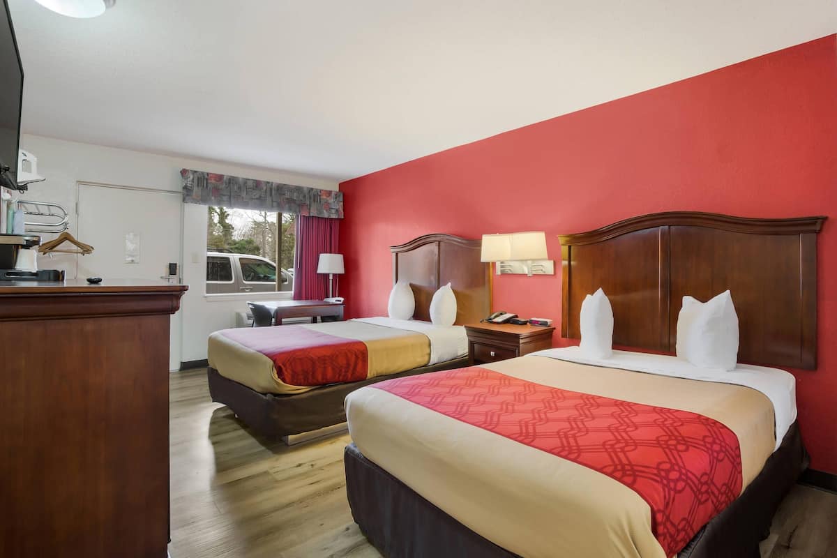 A hotel room with two beds, a desk, a chair, a lamp, and a window with curtains.