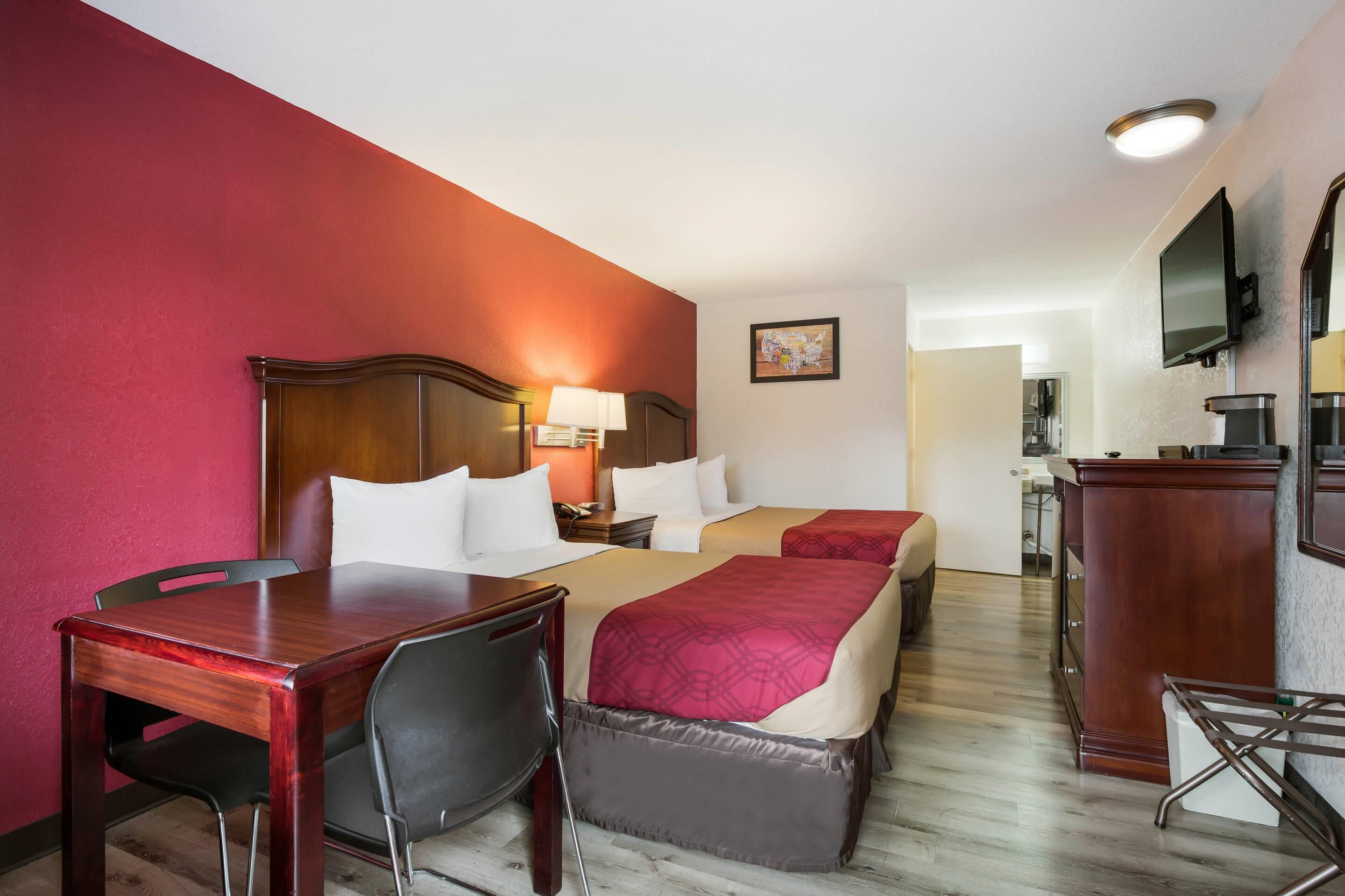 Una habitación de hotel con un escritorio de madera, dos camas, un televisor y una kitchenette.