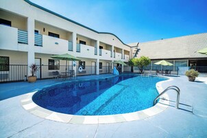 A swimming pool with a tiled deck, surrounded by a building with balconies and outdoor seating.