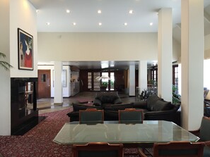 A spacious living area with a glass-top dining table, leather sofas, and a red patterned carpet. - Mikado Hotel - Universal Studios/Burbank (Valley Village)