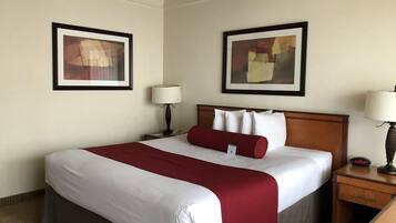 A hotel room with a large bed, two bedside tables, two wall-mounted lamps, and two framed abstract paintings.