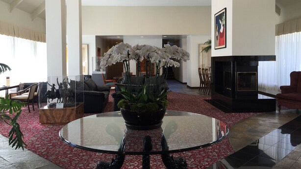 A modern living room with a glass coffee table, white orchids, a fireplace, and a dining area with chairs and a table. - Mikado Hotel - Universal Studios/Burbank (Valley Village)