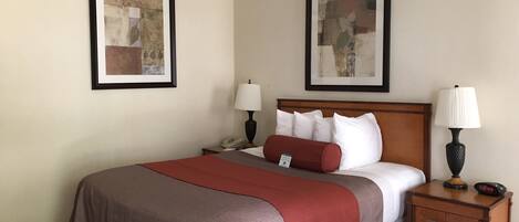 Une chambre d’hôtel avec un lit, deux tables de chevet, une petite table, une lampe et deux tableaux encadrés accrochés aux murs.