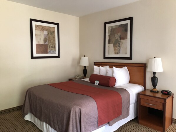 A hotel room with a bed, two bedside tables, a nightstand, a lamp, and two framed pictures on the walls.