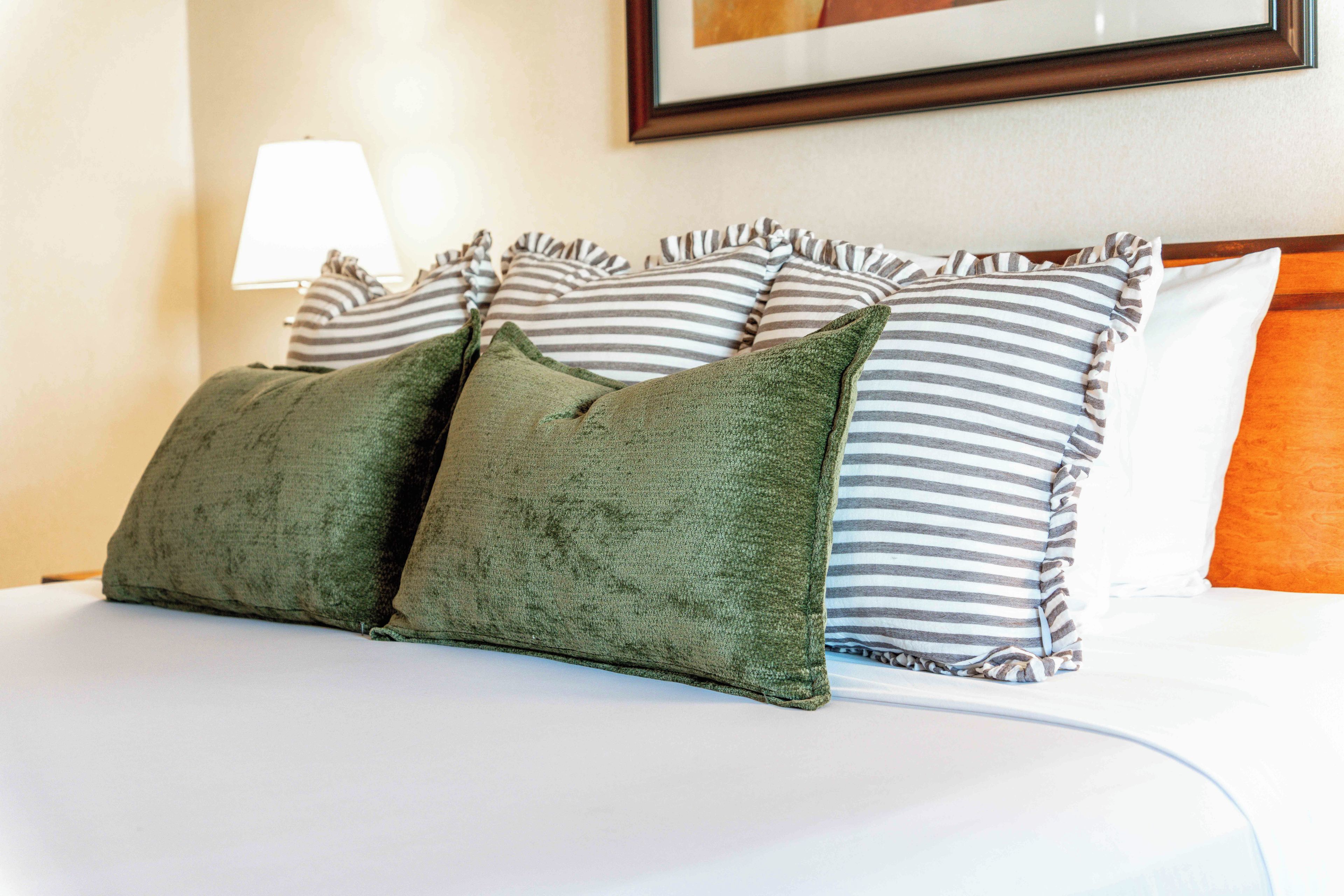 A bed with striped pillows and a green throw.
