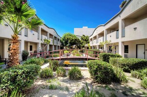 A courtyard with a red bridge, palm trees, and a water feature surrounded by greenery.