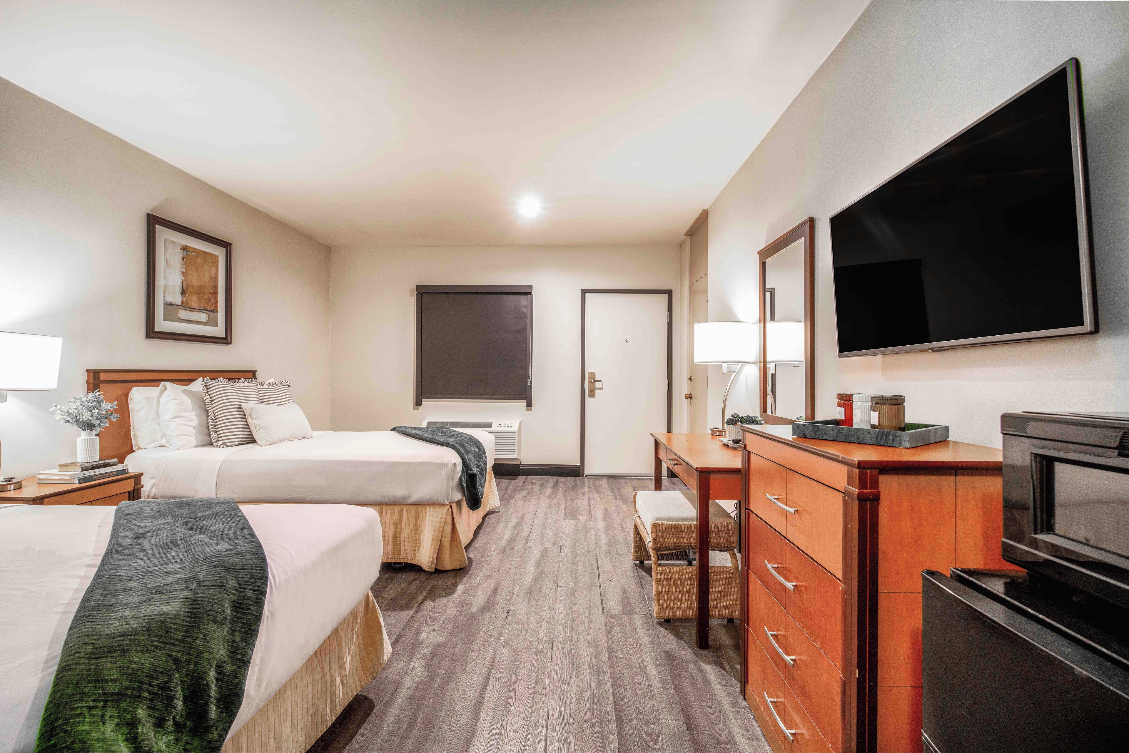 A hotel room with two beds, a desk, a television, and a large window.