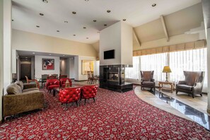 A spacious living room with a red patterned carpet, leather sofas, a fireplace, and a television mounted on the wall. - Mikado Hotel - Universal Studios/Burbank (Valley Village)