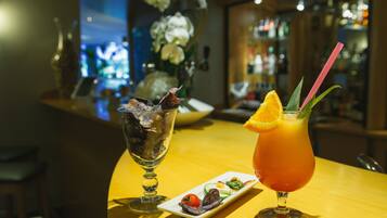 Un bar con un cóctel y un vaso de cubitos de hielo, un pequeño plato de aperitivos y un jarrón con flores al fondo.