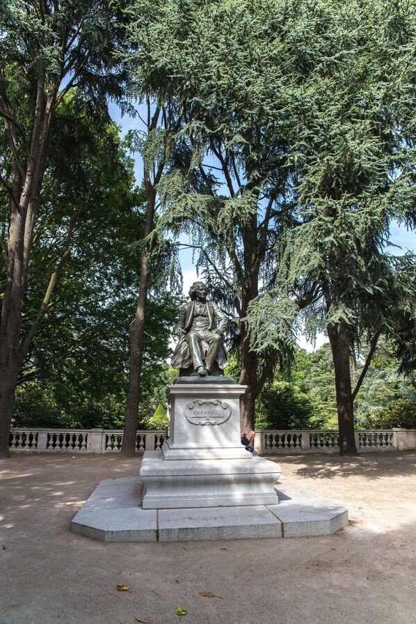 A statue of two figures seated on a pedestal in a park with trees and a fence in the background.
