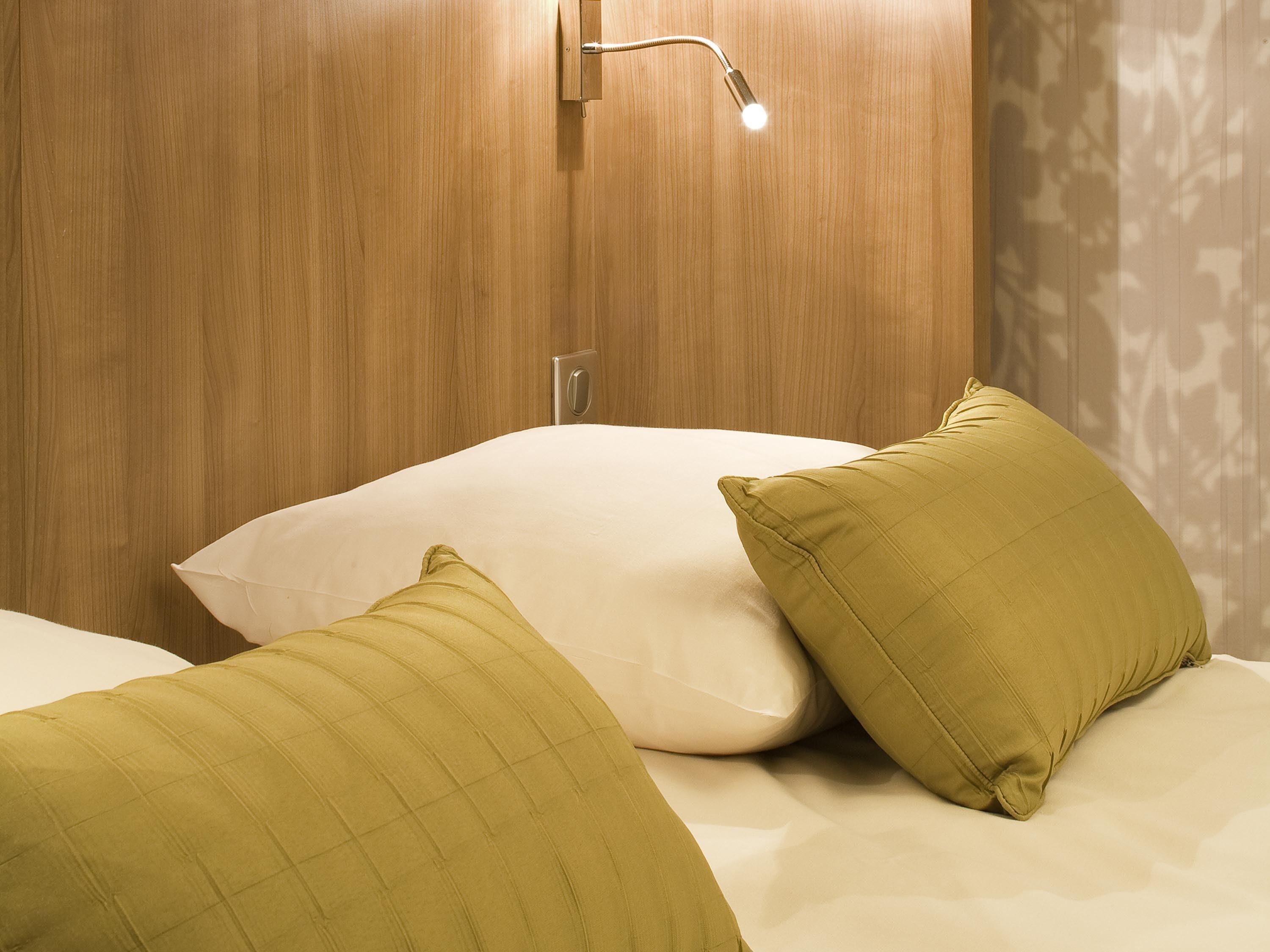 Una habitación de hotel con cabecera de madera, una lámpara de noche y dos almohadas.