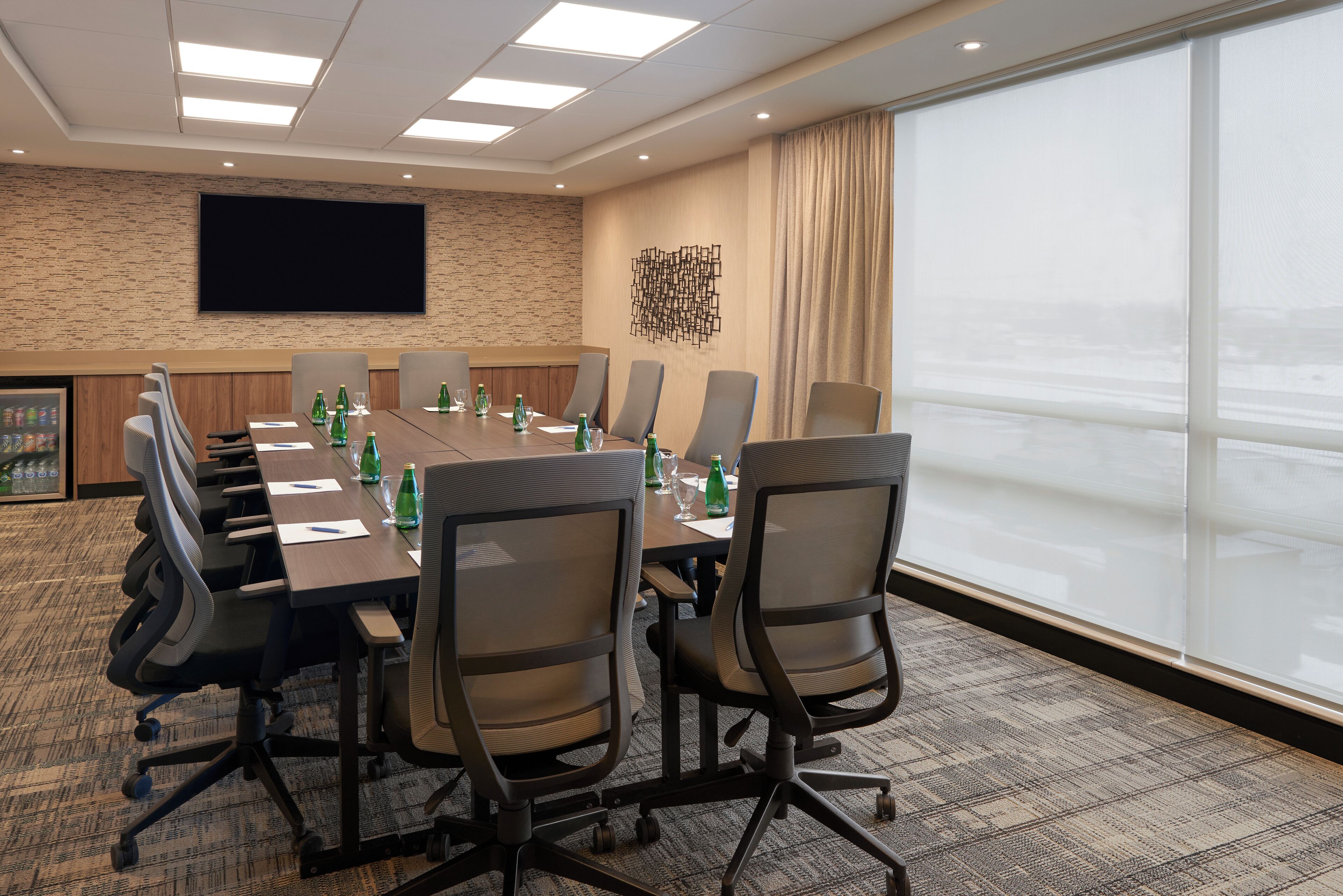A conference room with a long table, chairs, a flat-screen TV, and a large window.