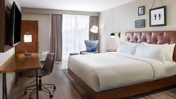 A hotel room with a large bed, a desk with a chair, a television, and a window with curtains.