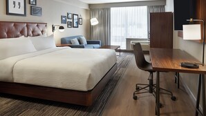 A hotel room with a large bed, a desk, a chair, and a sofa. There are framed pictures on the wall and a window with curtains. - Four Points by Sheraton Point Edward Sarnia (Sarnia)