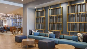 A modern lounge area with a blue sofa set, round wooden tables, and a decorative wall with vertical panels. - Four Points by Sheraton Point Edward Sarnia (Sarnia)