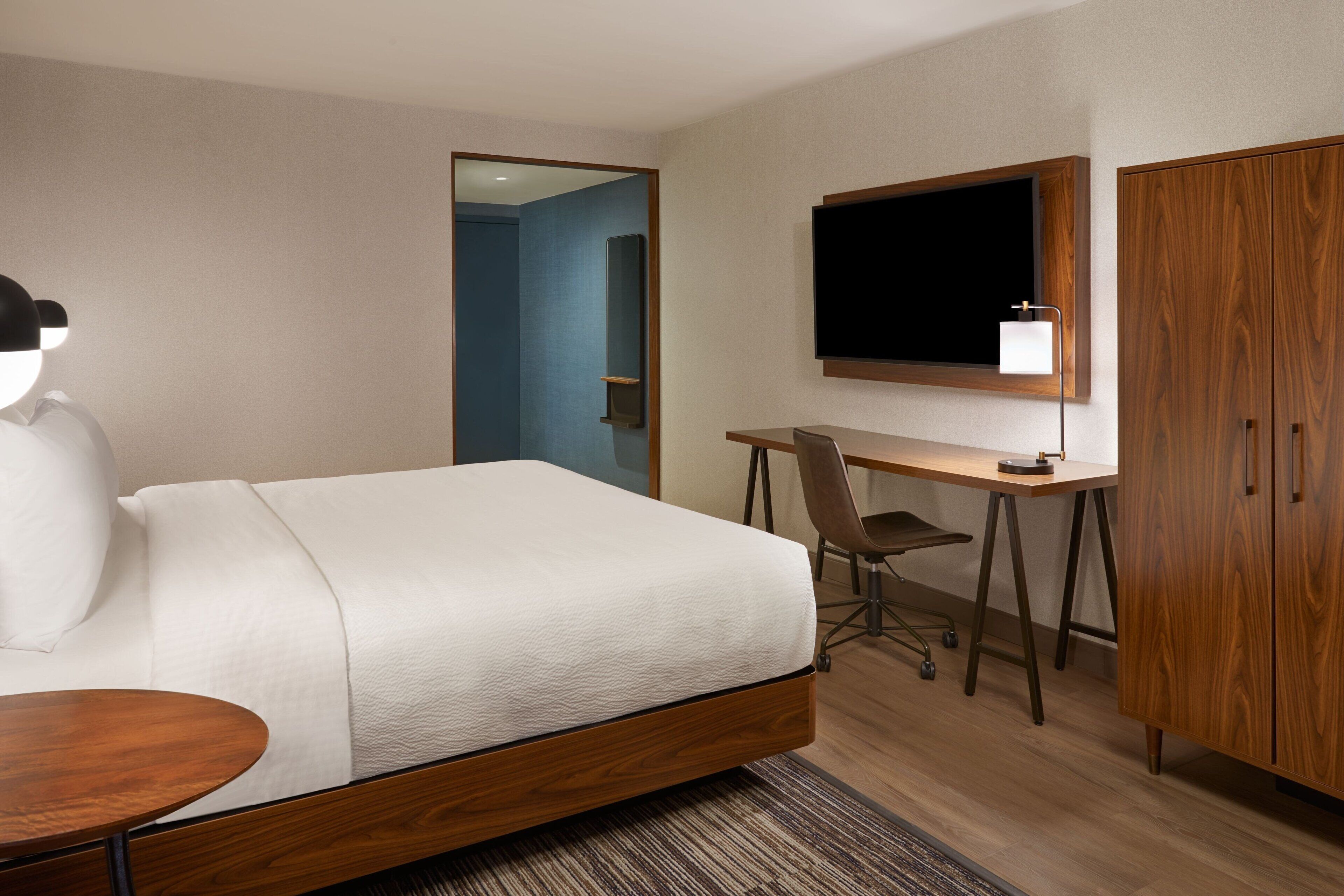 A hotel room with a bed, desk, chair, TV, and wardrobe.