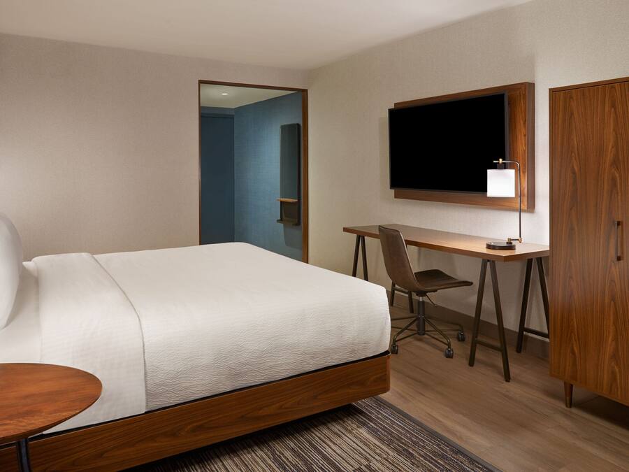 A hotel room with a bed, desk, chair, TV, and wardrobe.