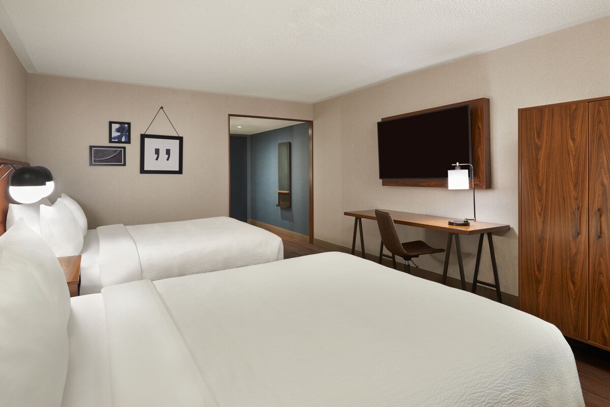 A hotel room with two beds, a desk, a chair, a TV, and a wardrobe.