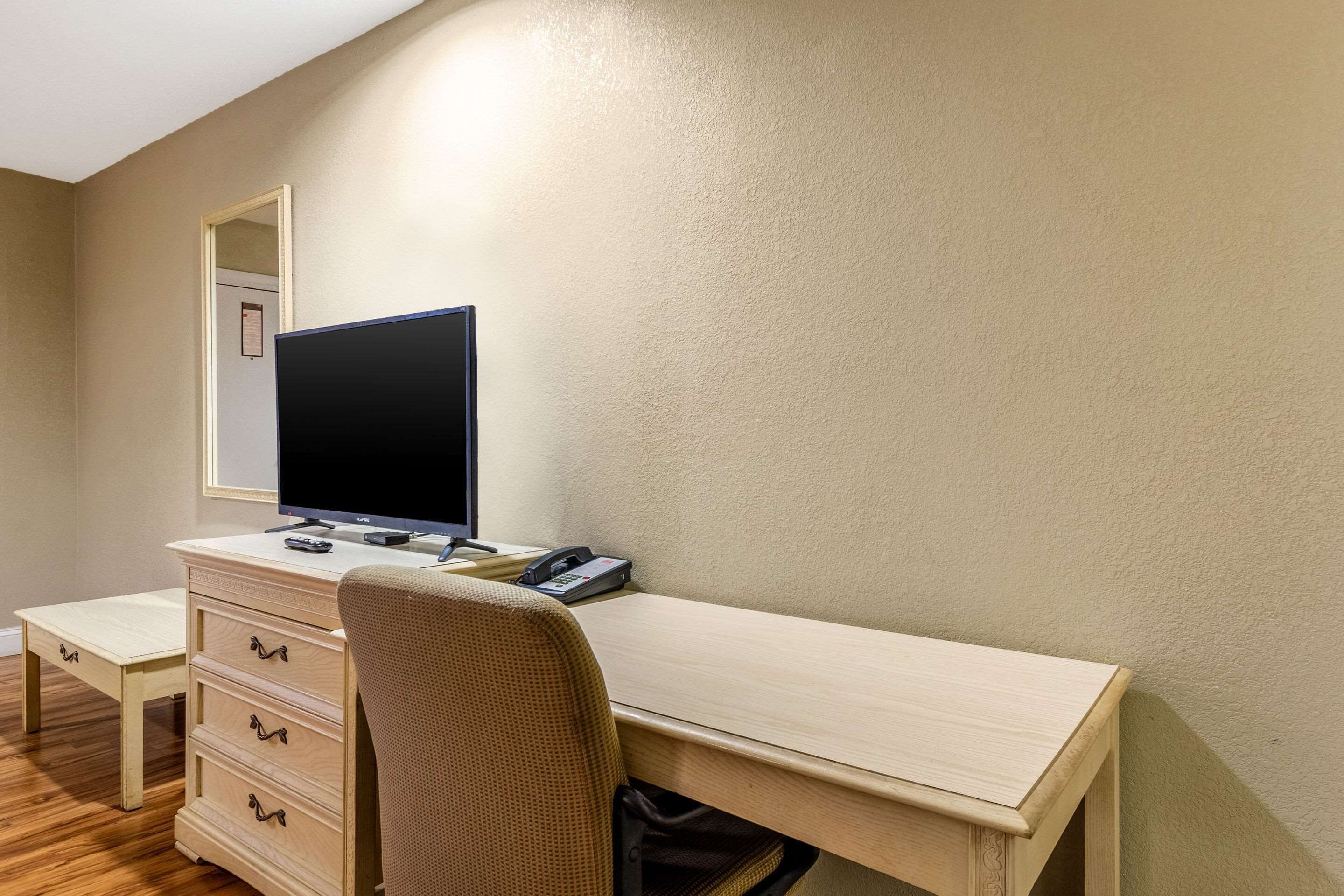 A hotel room with a wooden desk, a chair, a television, a telephone, and a mirror.