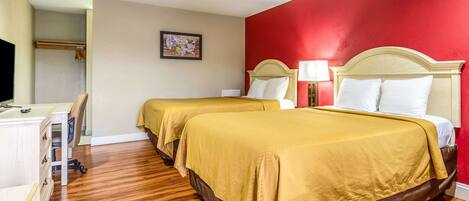 Habitación de hotel con dos camas, suelo de madera, un escritorio y una pared decorada en rojo.