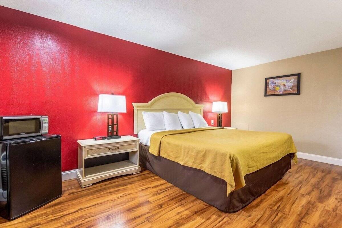A hotel room with a bed, nightstand, lamp, and a small refrigerator.