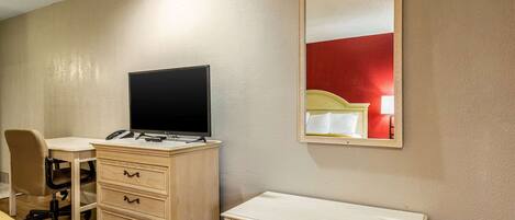 A bedroom with a bed, a desk with a computer, a chair, a dresser, and a mirror on the wall.