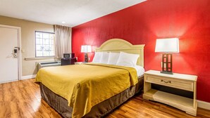 A hotel room with a bed, bedside tables, a heater, and a window with curtains.