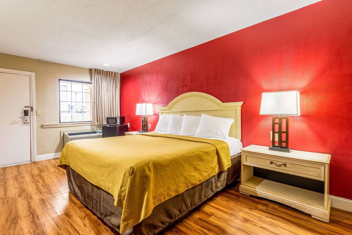 A hotel room with a bed, bedside tables, a heater, and a window with curtains.