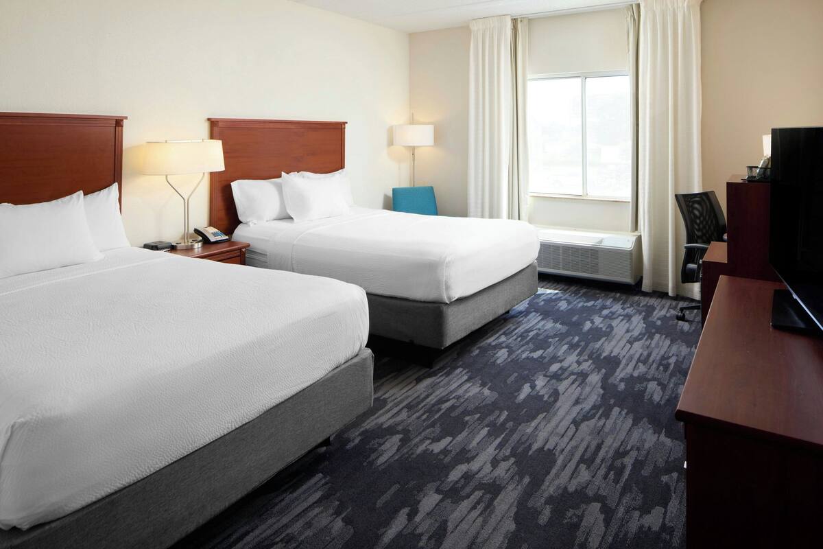 A hotel room with two beds, a desk, a television, and a window with curtains.