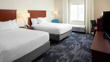 A hotel room with two beds, a desk, a television, and a window with curtains.