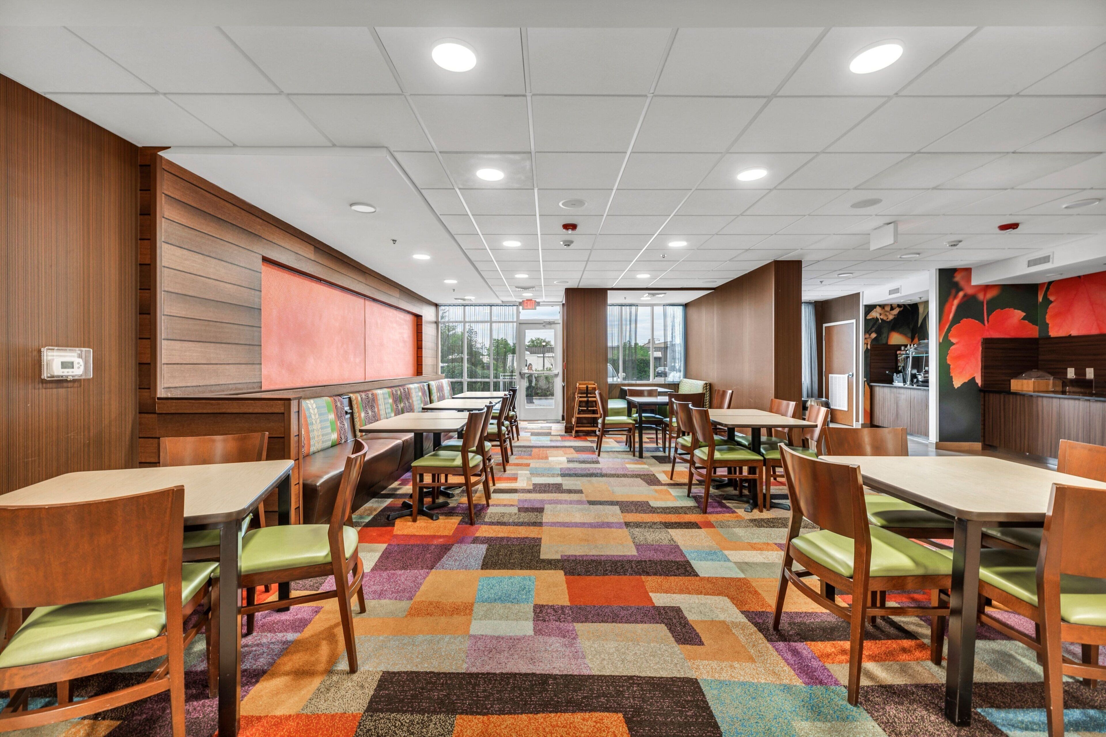 A restaurant with booths and tables, a patterned carpet, and a view through the windows.