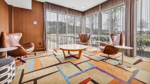 Un moderno vestíbulo de hotel con sillones de cuero, una mesa redonda y ventanas amplias con vistas al estacionamiento.