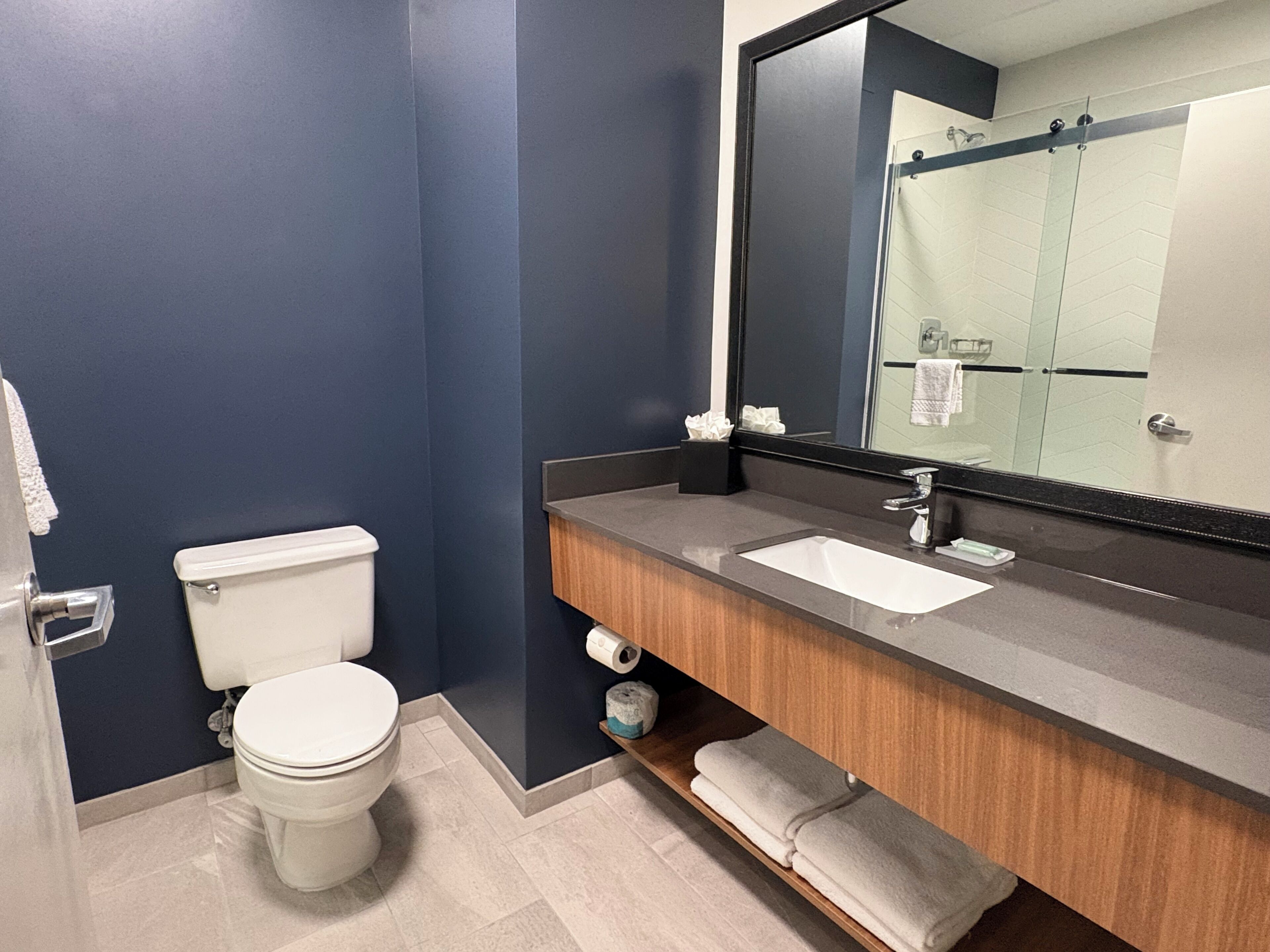 Un baño moderno con inodoro, lavamanos, espejo y toallero.