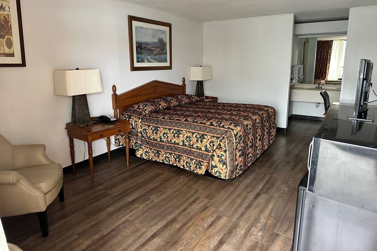 A hotel room with a wooden bed, two bedside tables with lamps, a chair, a desk, a mirror, and a television.