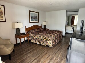 Une chambre d’hôtel avec un lit en bois, deux tables de chevet avec des lampes, une chaise, un bureau, un miroir et un téléviseur.