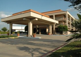 Um hotel com entrada coberta, vários andares e um pátio central com vasos de plantas.