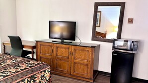Ein Hotelzimmer mit einem Bett, einem Holzschrank mit Fernseher, einem Schreibtisch, einem Sessel, einer Mikrowelle und einem Spiegel.